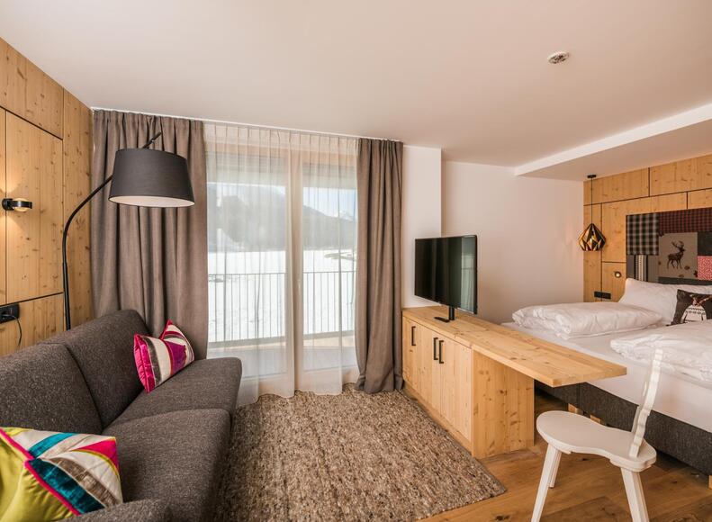 "Family Flora" Zimmer mit Sofa, TV, Minikühlschrank, Doppelbett und Balkon Richtung Innichen