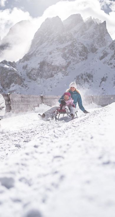 Una famiglia con due bambini percorre una pista da slittino in slitta nel comprensorio sciistico delle tre cime