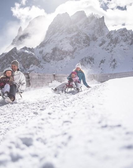 Eine Familie mit zwei Kindern fährt mit dem Schlitten eine Rodelbahn im Skigebiet Drei Zinnen entlang