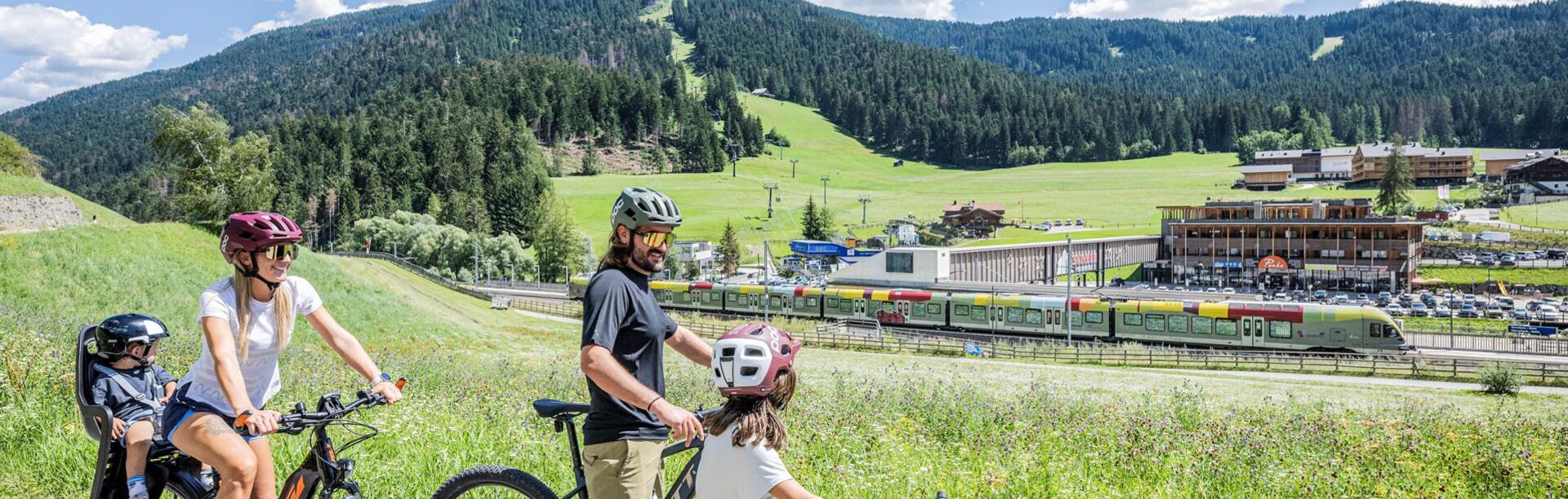 Eine Familie fährt mit ihren Fahrrädern einen Fahrradweg entlang, daneben fährt der Zug vorbei