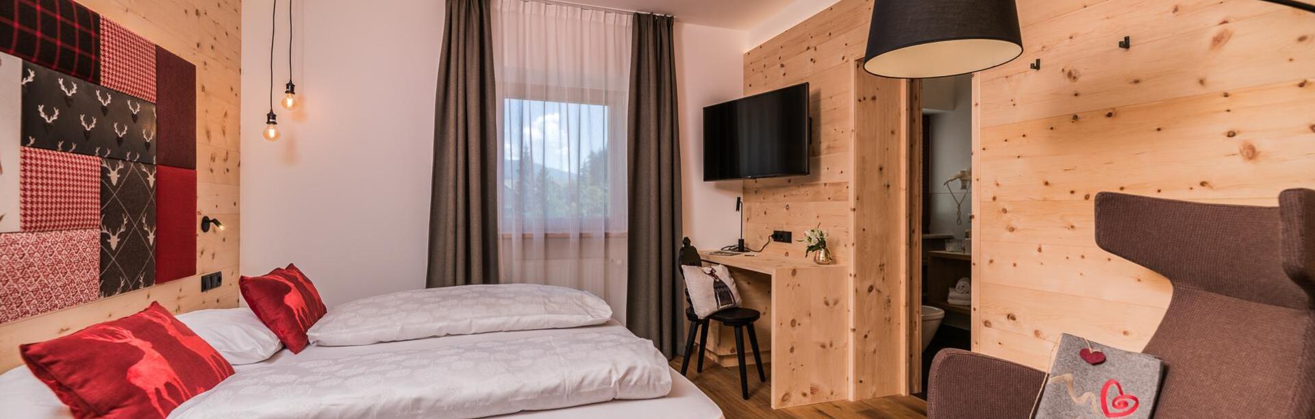 Cirmolino room with bed, TV, mini fridge and window facing the street / the village of Versciaco