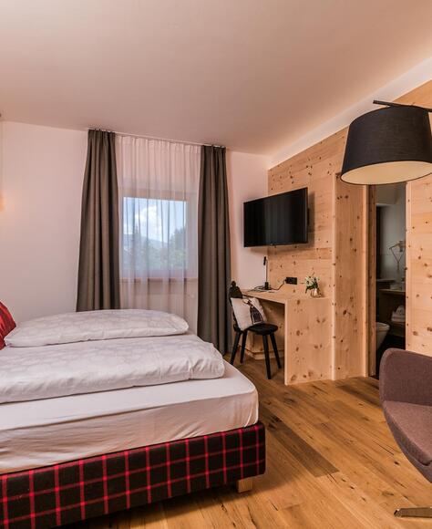 Zimmer Cirmolino mit Bett, TV, Minikühlschrank und Fenster zur Straße / zum Dorf Versciaco