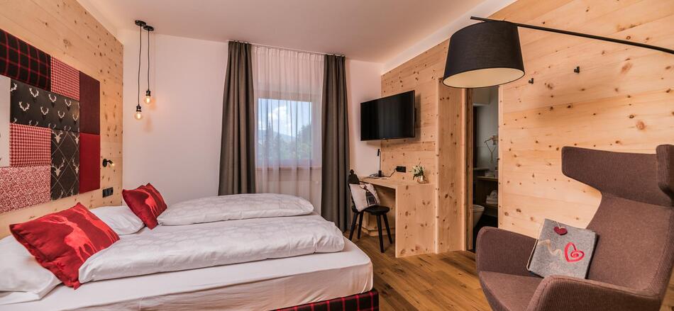 Zimmer Cirmolino mit Bett, TV, Minikühlschrank und Fenster zur Straße / zum Dorf Versciaco