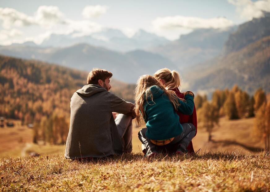 Una famiglia è seduta su un prato e guarda il paesaggio montano autunnale