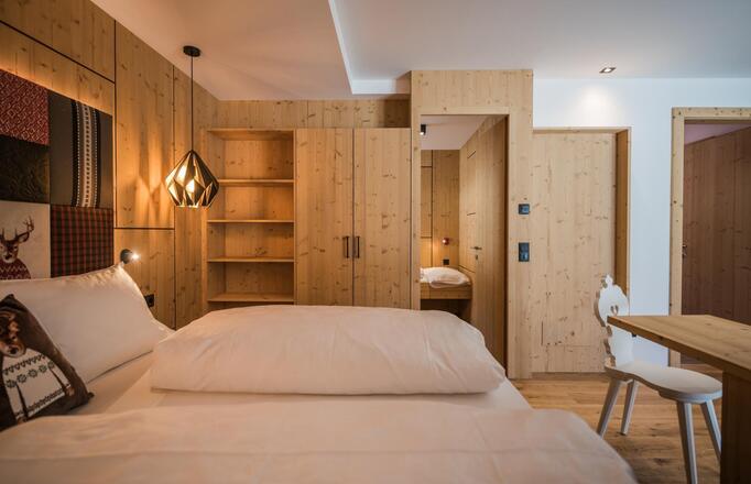 Zimmer „Family Flora“ mit Doppelbett, Bücherregal, Kleiderschrank, separatem Kinderbereich und Schreibtisch