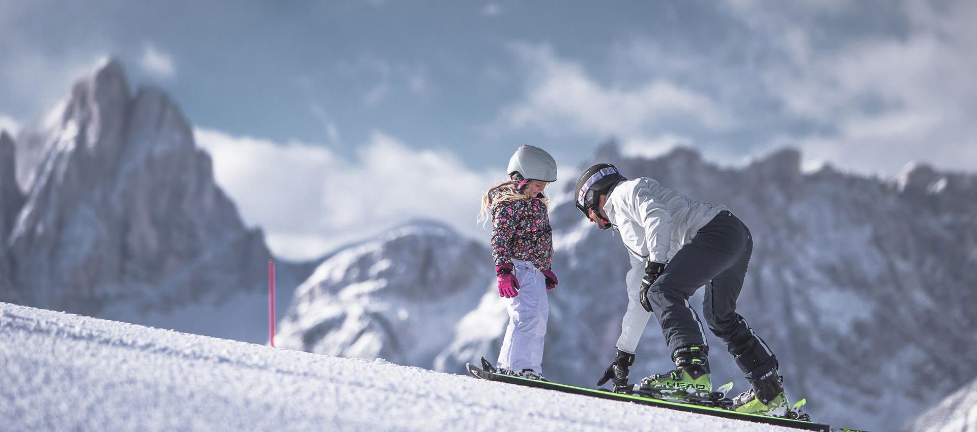 A man is teaching a child how to ski in the Drei Zinnen ski area