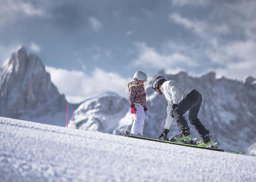 A man is teaching a child how to ski in the Drei Zinnen ski area