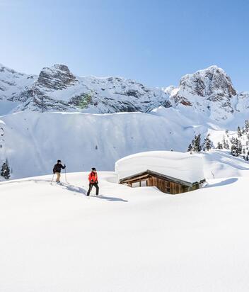 Two people are snowshoeing in Prags, surrounded by the Dolomites