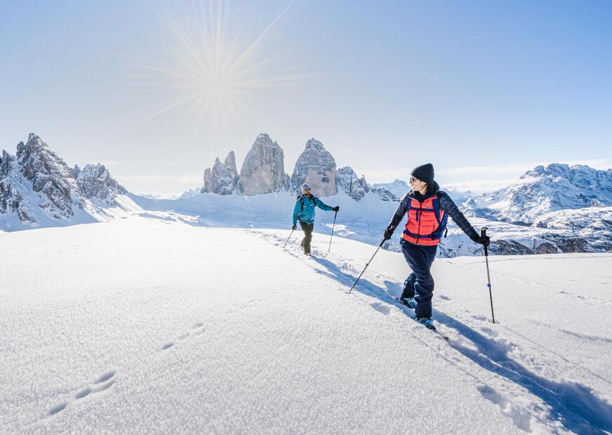 Due persone sono impegnate in un’escursione con le ciaspole, sullo sfondo si ergono le tre cime