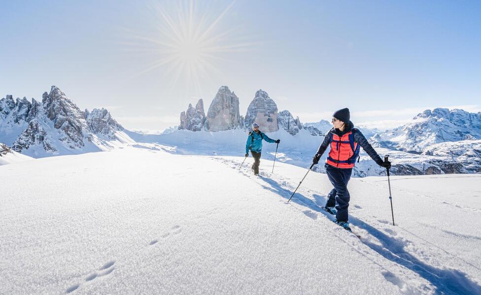 Due persone sono impegnate in un’escursione con le ciaspole, sullo sfondo si ergono le tre cime