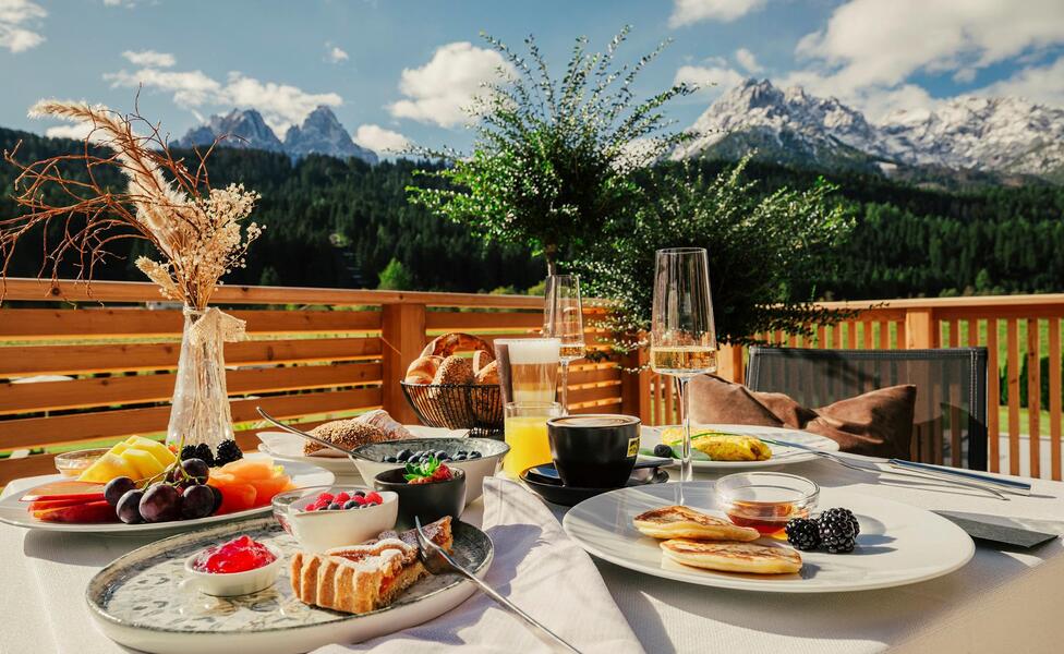 Breakfast with cold and hot beverages as well as sweet and savory food on the terrace with the Haunold on the background