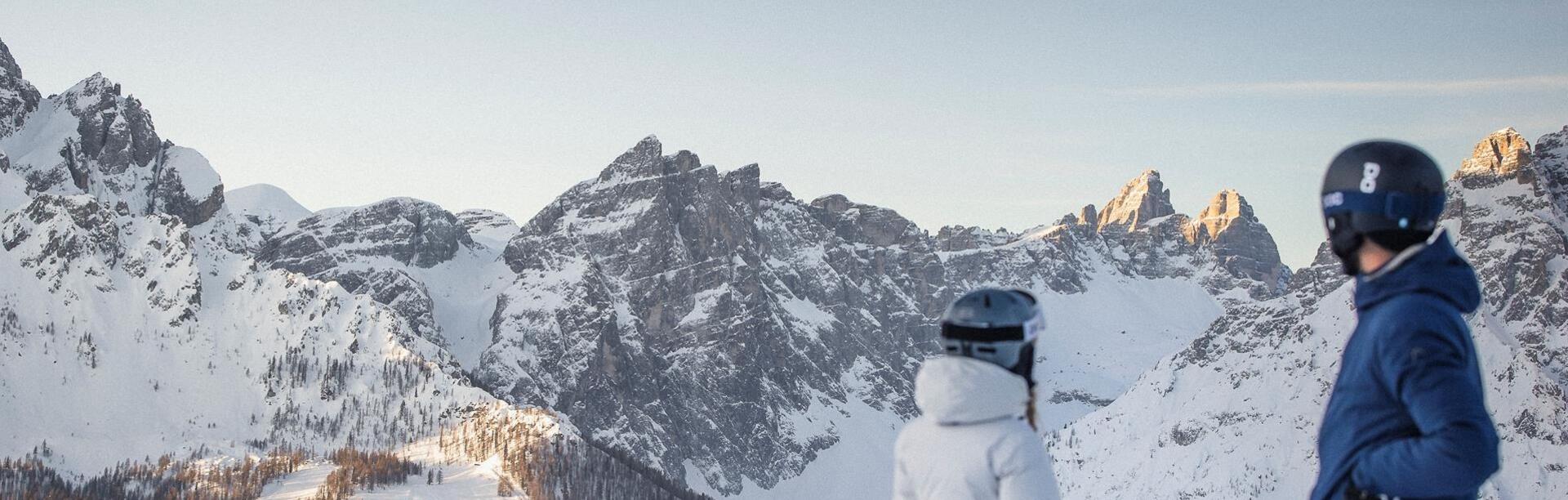 Un uomo e una donna vestiti da sci guardano le Dolomiti nella zona sciistica delle Tre Cime