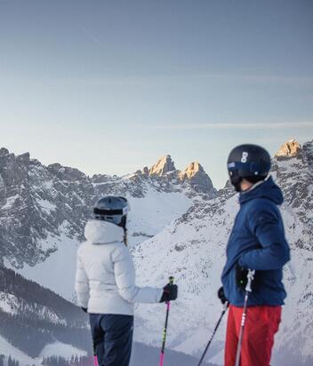 A man and a woman dressed in ski clothing look at the Dolomites in the Three Peaks ski area.