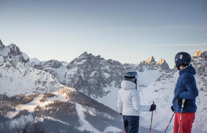 A man and a woman dressed in ski clothing look at the Dolomites in the Three Peaks ski area.