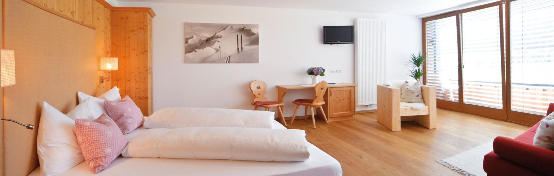 Superior room with double bed, sofa, desk, wardrobe and balcony looking to Innichen