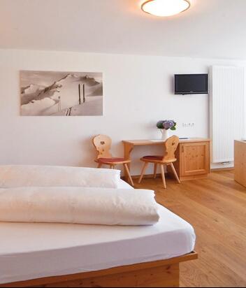 Superior room with double bed, sofa, desk, wardrobe and balcony looking to Innichen