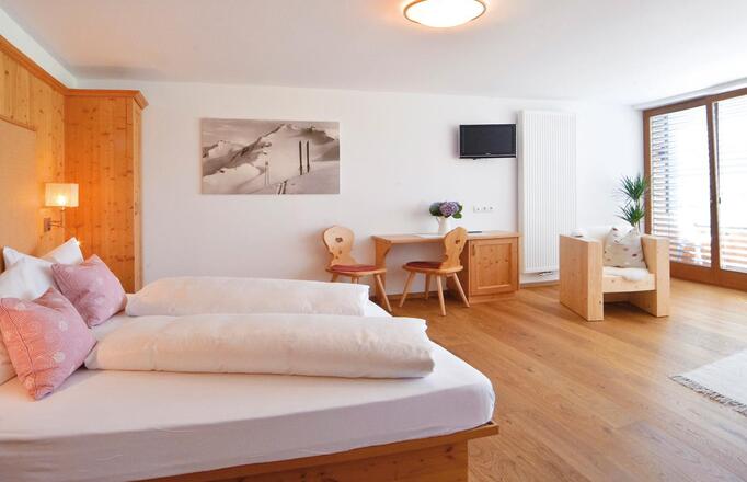 Superior room with double bed, sofa, desk, wardrobe and balcony looking to Innichen
