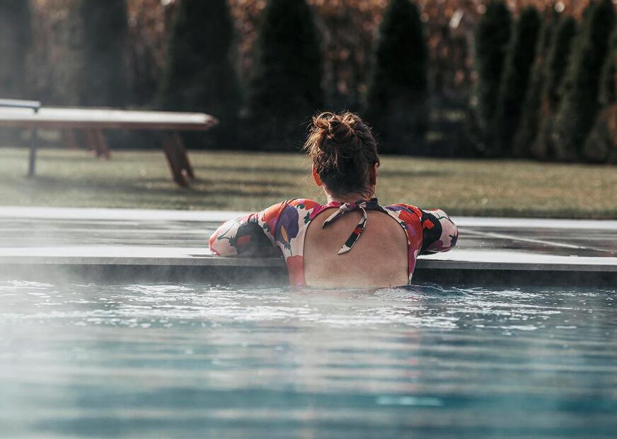 Una donna a bordo piscina con un lettino e ombrellone aperto sullo sfondo