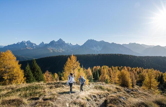 Zwei Personen wandern im Herbst, im Hintergrund sieht man die Dolomiten