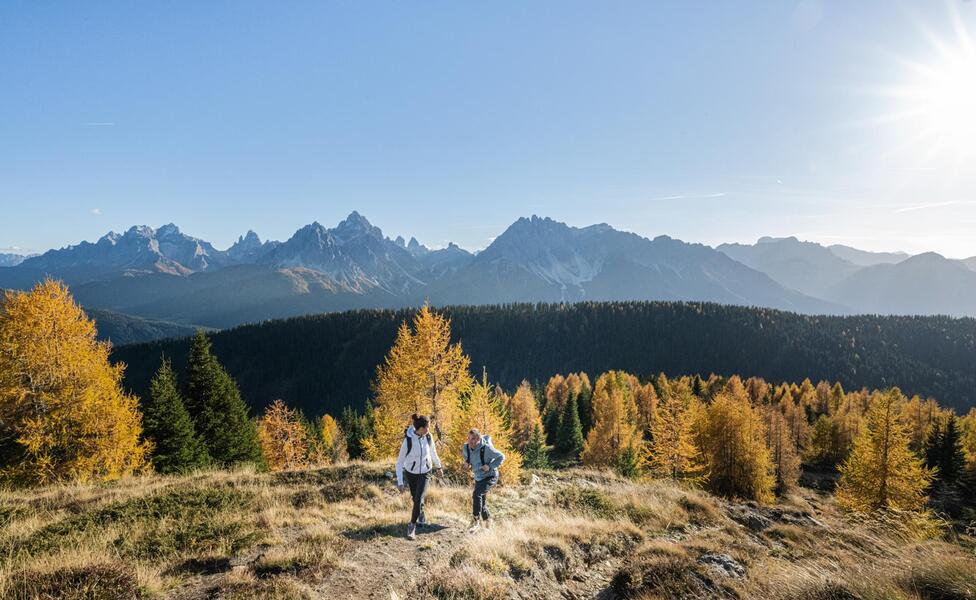 Due persone fanno un’escursione in autunno; sullo sfondo si vedono le Dolomiti