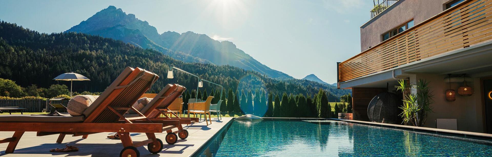 Schwimmbad vom Helmhotel mit Liegen, Tischen und Stühlen, Garten und Haundold im Hintergrund