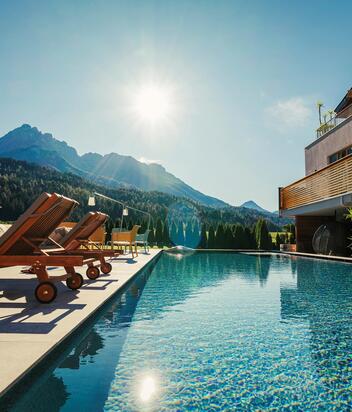 Swimmingpool of the Helmhotel with sun loungers, small tables and chairs, the garden and the Haunold on the backside