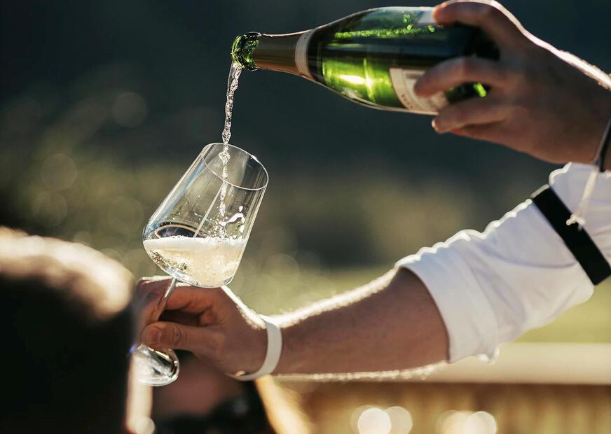 Un uomo versa un calice di vino bianco a un uomo e a una donna