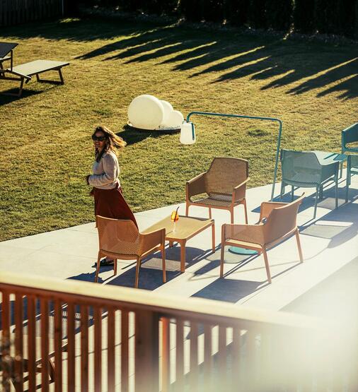 A lady in a garden with some small tables and chairs and the edge of a swimming pool